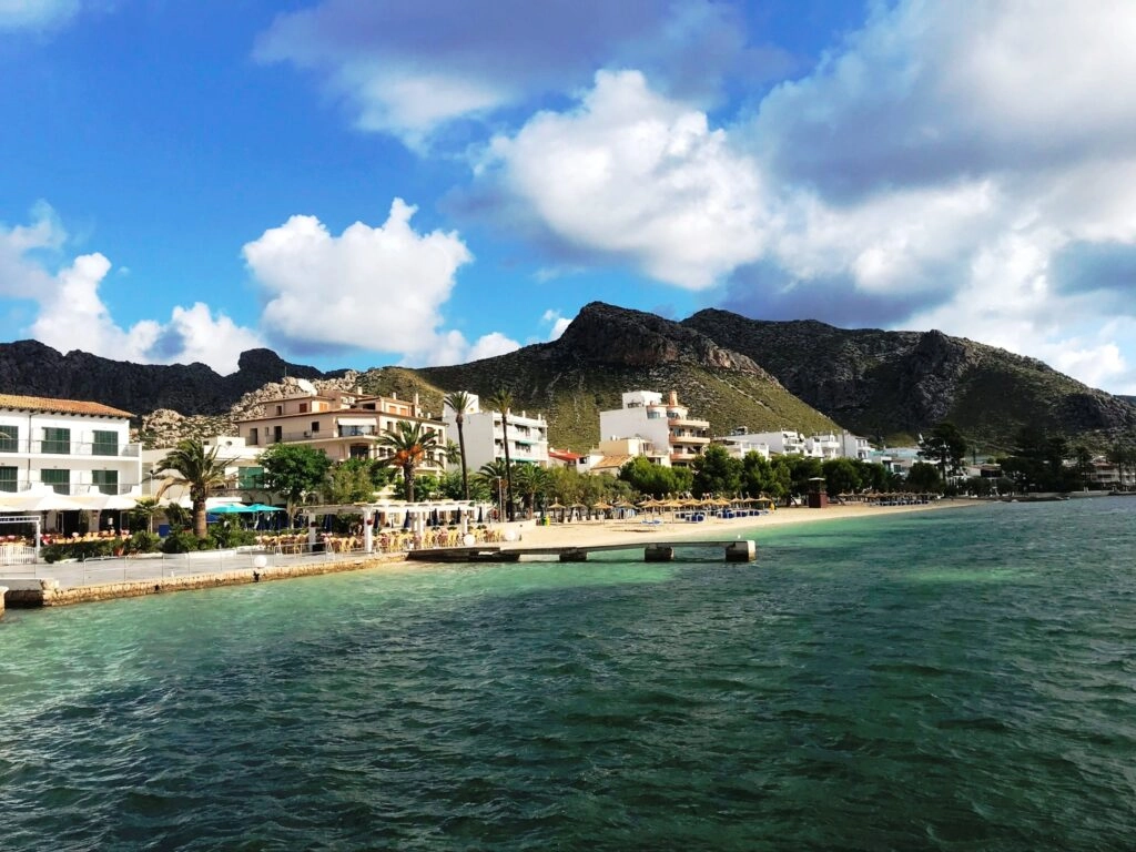Uitzicht over de boulevard en het strand van Port de Pollença op Mallorca, met helderblauw water en groene bergen op de achtergrond