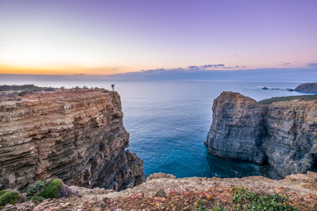 Wandelaar op de kliffen van de Fisherman’s Trail langs de Atlantische kust van Portugal bij zonsondergang – onderdeel van de Rota Vicentina tussen Alentejo en Algarve.
