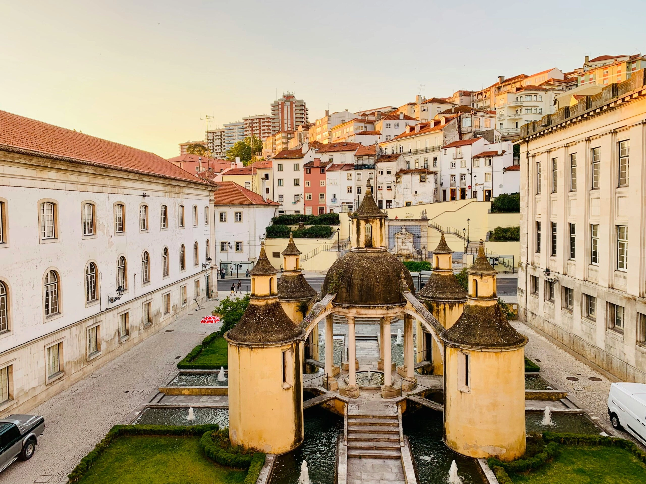 Fonte dos Jardins da Manga in het historische centrum van Coimbra, omringd door klassieke gebouwen bij zonsondergang.
