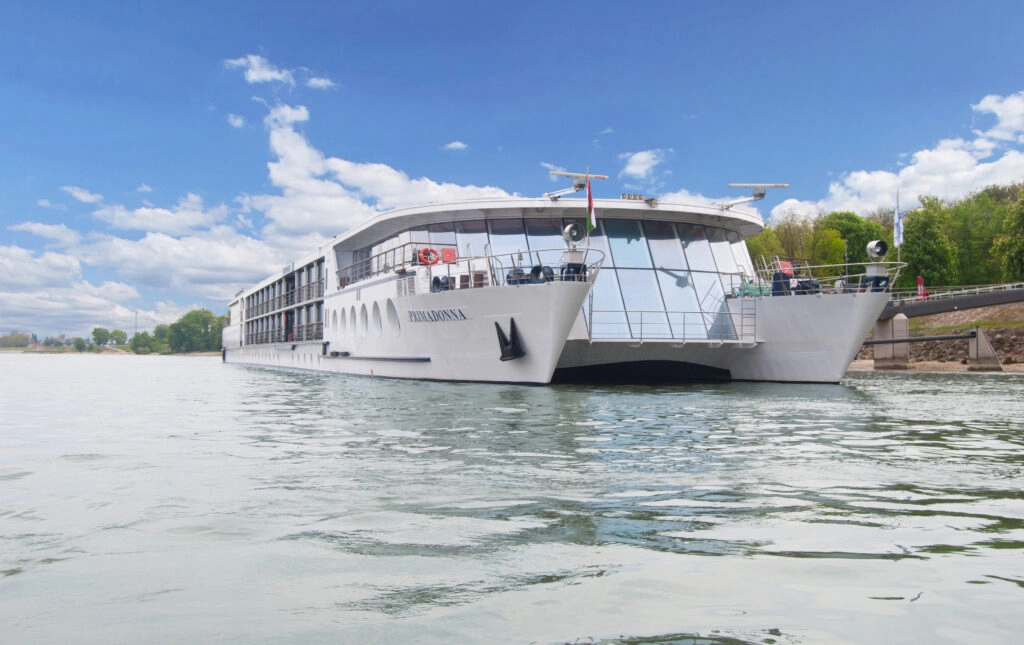 De MS Primadonna, een elegant catamaranschip, vaart over de Donau omgeven door een helderblauwe lucht en groene oevers.