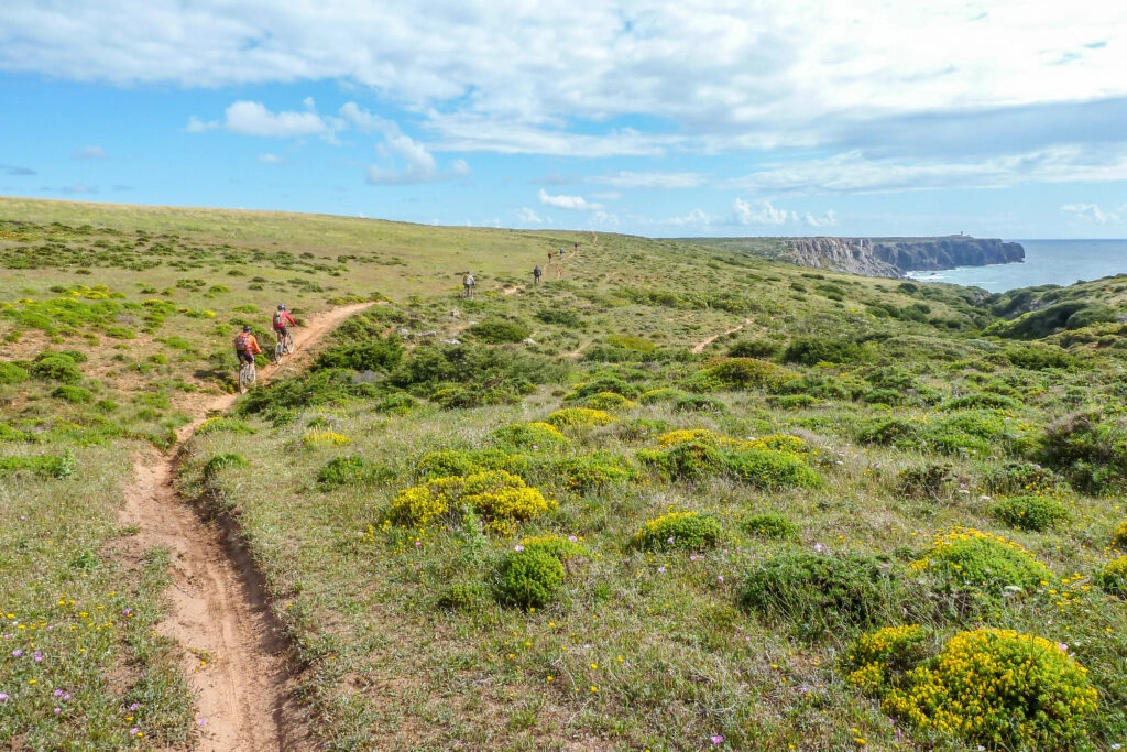 Mountainbikers op een singletrack langs de Costa Vicentina richting Sagres, met uitzicht op Cabo de São Vicente – het zuidwestelijkste punt van Portugal.
