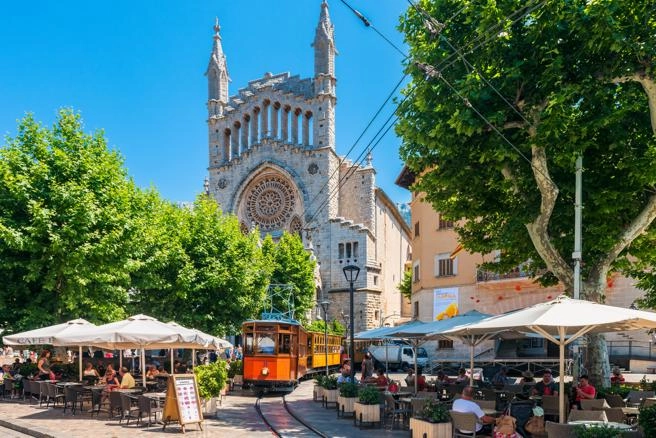 De historische tram van Sóller rijdt over het levendige plein voor de Sant Bartomeu-kerk op Mallorca.