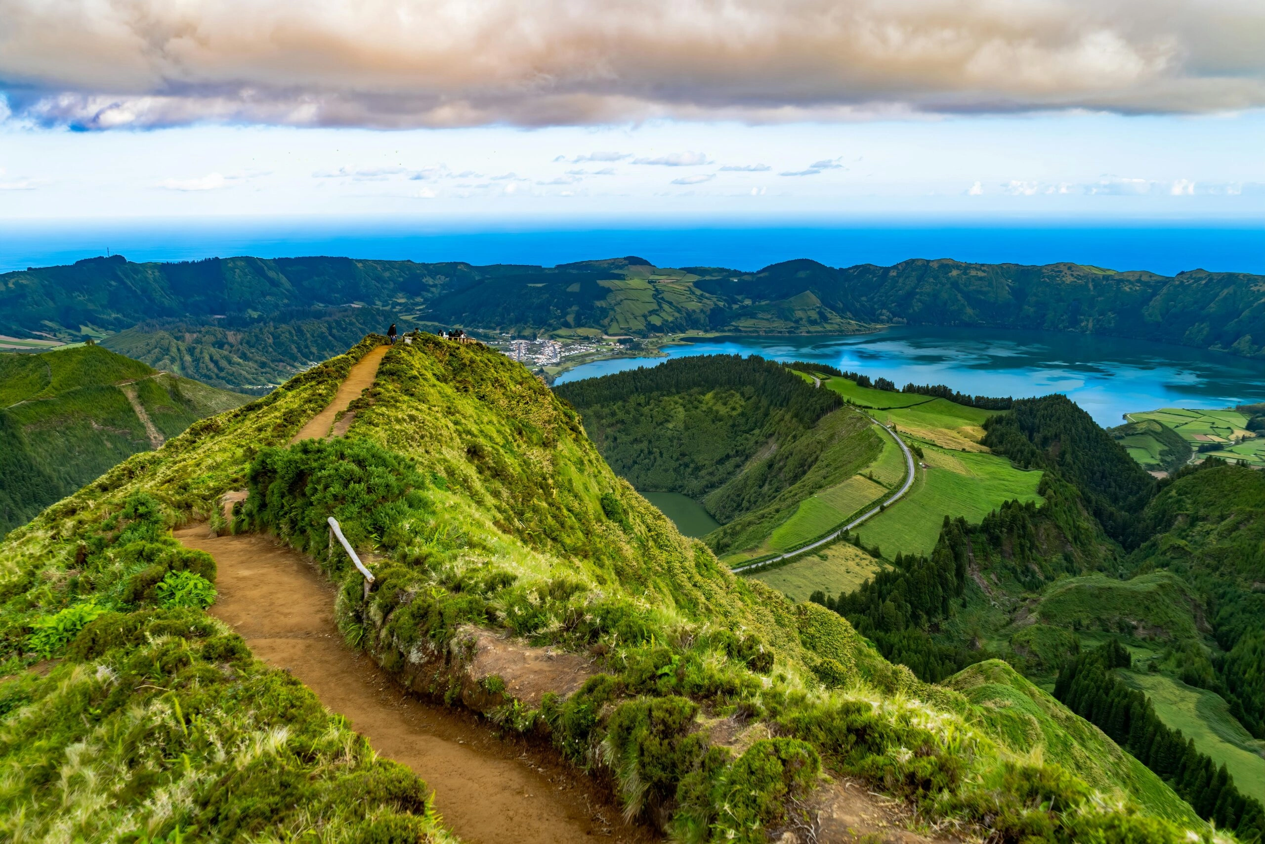 Smal bergpad op de Azoren met uitzicht op groene kraterlandschappen en het blauwgroene meer van Sete Cidades.