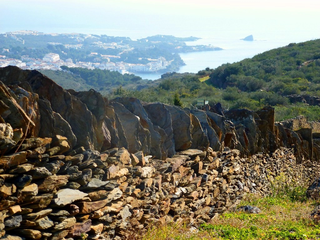 Droge-stenen muur op Cap de Creus met uitzicht op de baai en witte huizen van Cadaqués aan de Costa Brava.