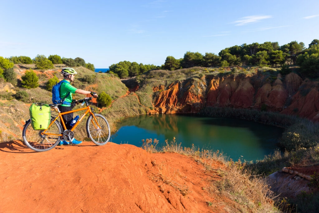 Fietser bij de Cava di Bauxite nabij Otranto, Puglia, met rode aarde, groen meer en uitzicht over de Adriatische Zee.