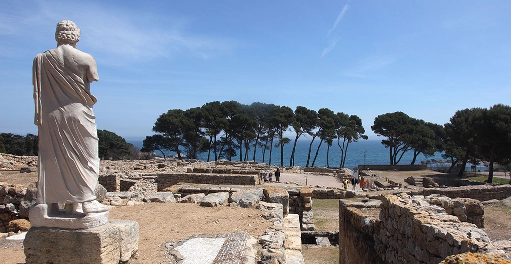 Uitzicht op de Grieks-Romeinse ruïnes van Empúries met een standbeeld op de voorgrond en de Middellandse Zee op de achtergrond.