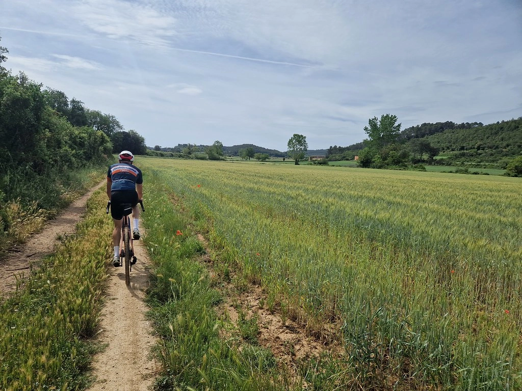 Gravelbiker rijdt over een smal pad door groene velden in de Empordà-regio van de Costa Brava.