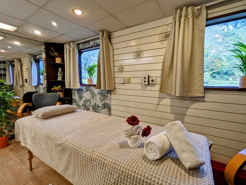 Massagesalon aan boord van de MS Prinzessin Katharina met massagetafel, decoratieve elementen en uitzicht op de Donau.