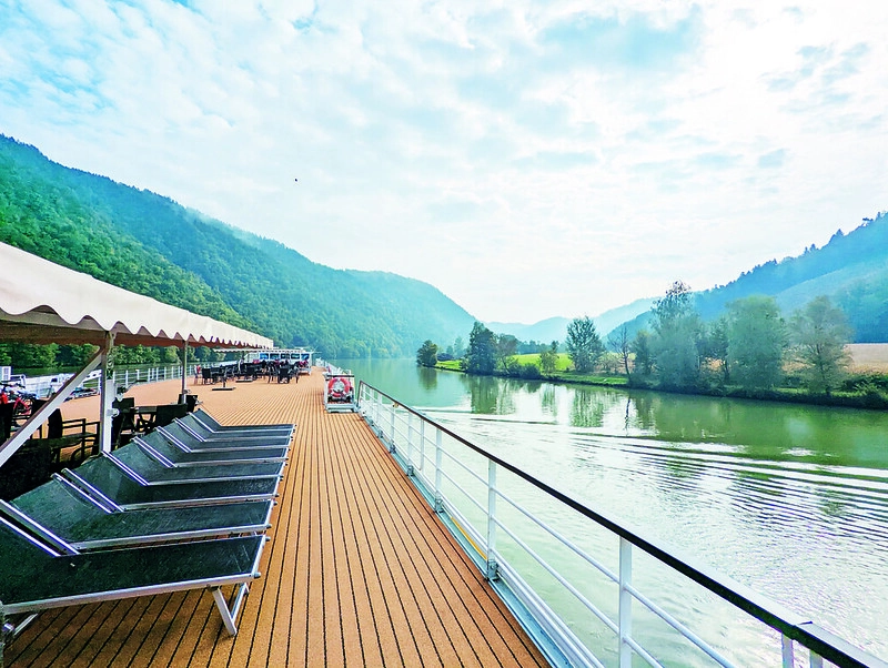 Zonnedek van de MS Prinzessin Katharina met ligstoelen en panoramisch uitzicht over de Donau en groene heuvels.