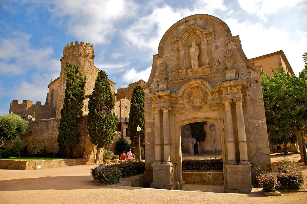 Middeleeuwse toegangspoort met kasteelmuur en cipressen in het historische dorp Peratallada in Catalonië.