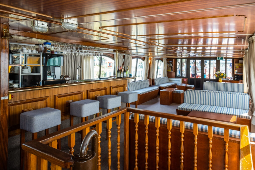 Loungebar van L’Estello met houten interieur, zithoeken en grote ramen langs het kanaal
