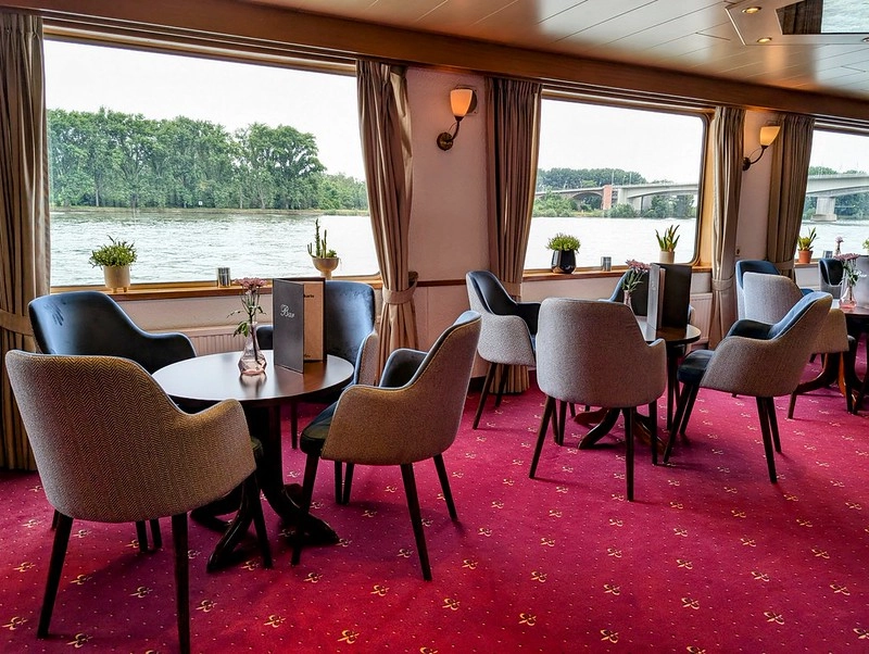 Gezellige lounge van MS Olympia met grote panoramavensters en uitzicht op de rivier