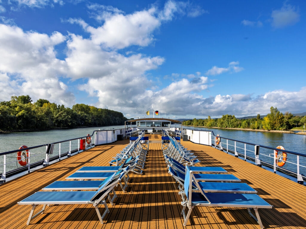 Zonnedek van MS Olympia met ligstoelen en panoramisch uitzicht over de Rijn tijdens een riviercruise.