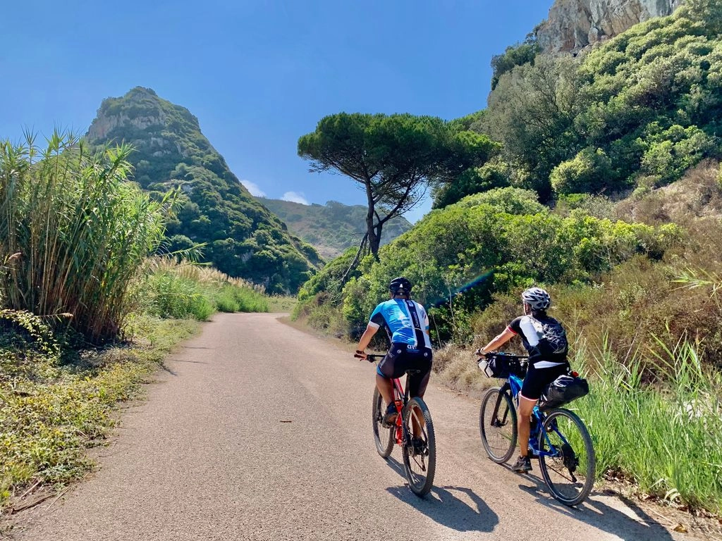 Twee fietsers rijden door een groene vallei langs bergen en mediterrane vegetatie tijdens een actieve fietsroute in Portugal.