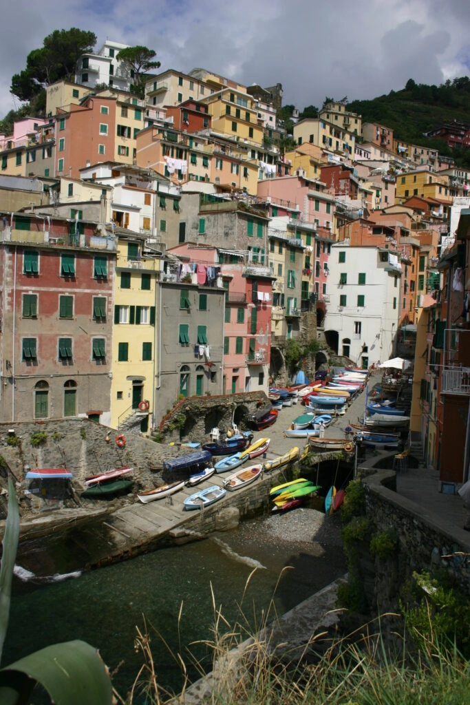 Kleine haven van Riomaggiore met kleurrijke huizen tegen de rotswand en traditionele vissersbootjes langs de kade.
