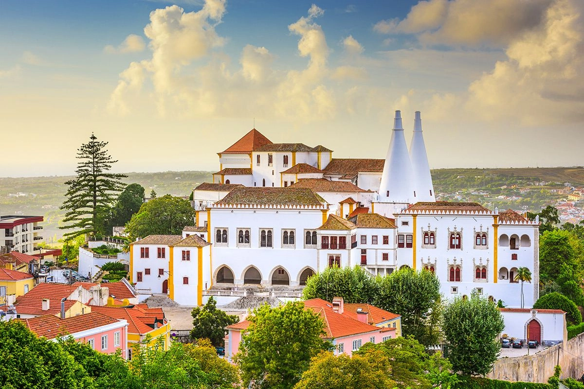 Het Palácio Nacional de Sintra met de iconische witte schoorstenen, gelegen in het historische centrum en omringd door groen en kleurrijke huizen.