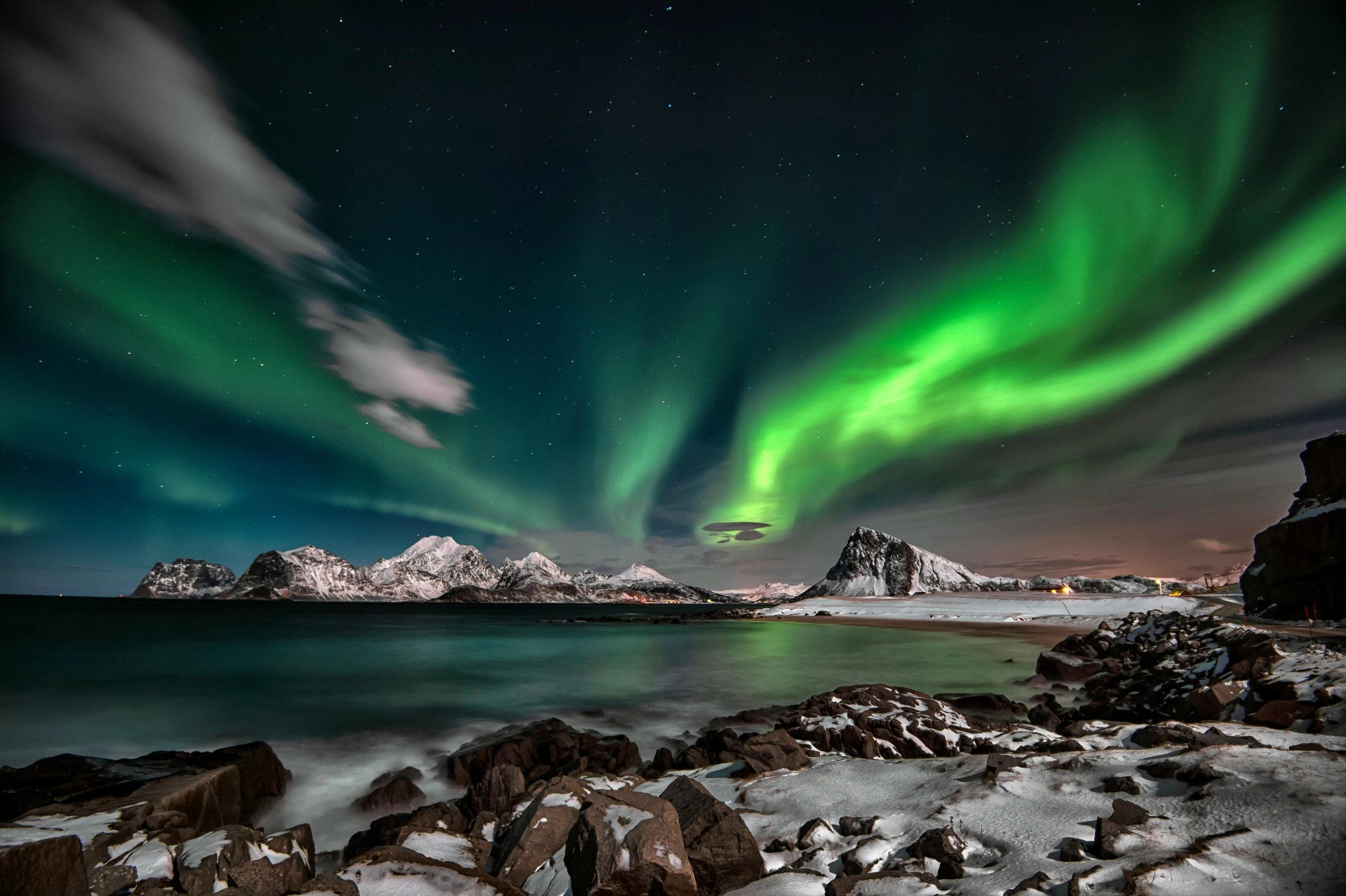 Noorderlicht boven de besneeuwde kust en bergen van de Lofoten in Scandinavië, een indrukwekkende coolcation vol natuur, rust en winterse beleving.