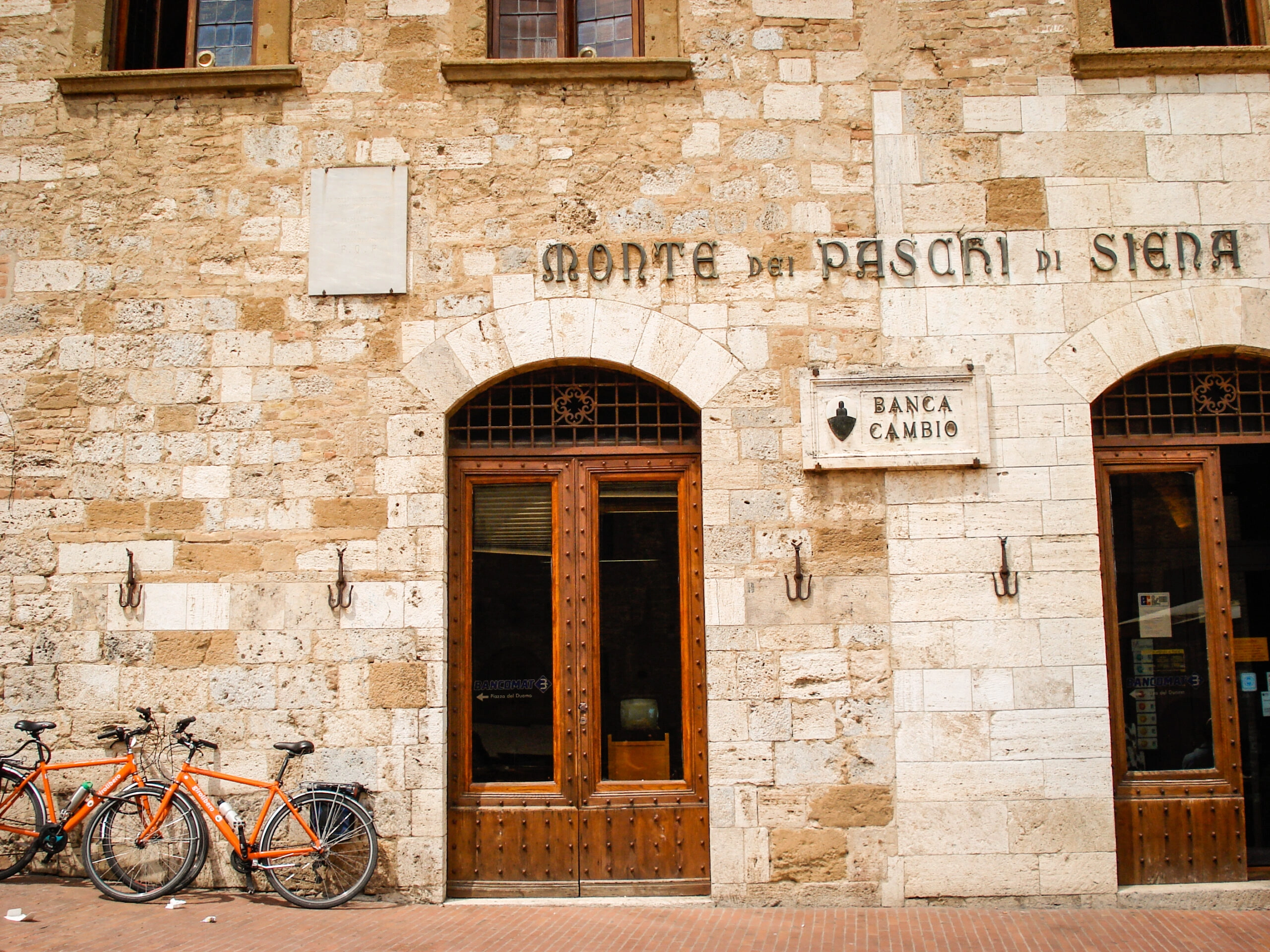 Two orange bicycles against the wall of Banca Monte dei Paschi di Siena, the world’s oldest bank, during a cycling holiday in Siena, Italy.