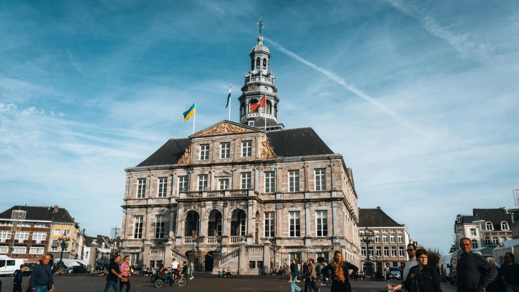 Het historische stadhuis van Maastricht op de Markt, met mensen op het plein onder een heldere blauwe lucht.