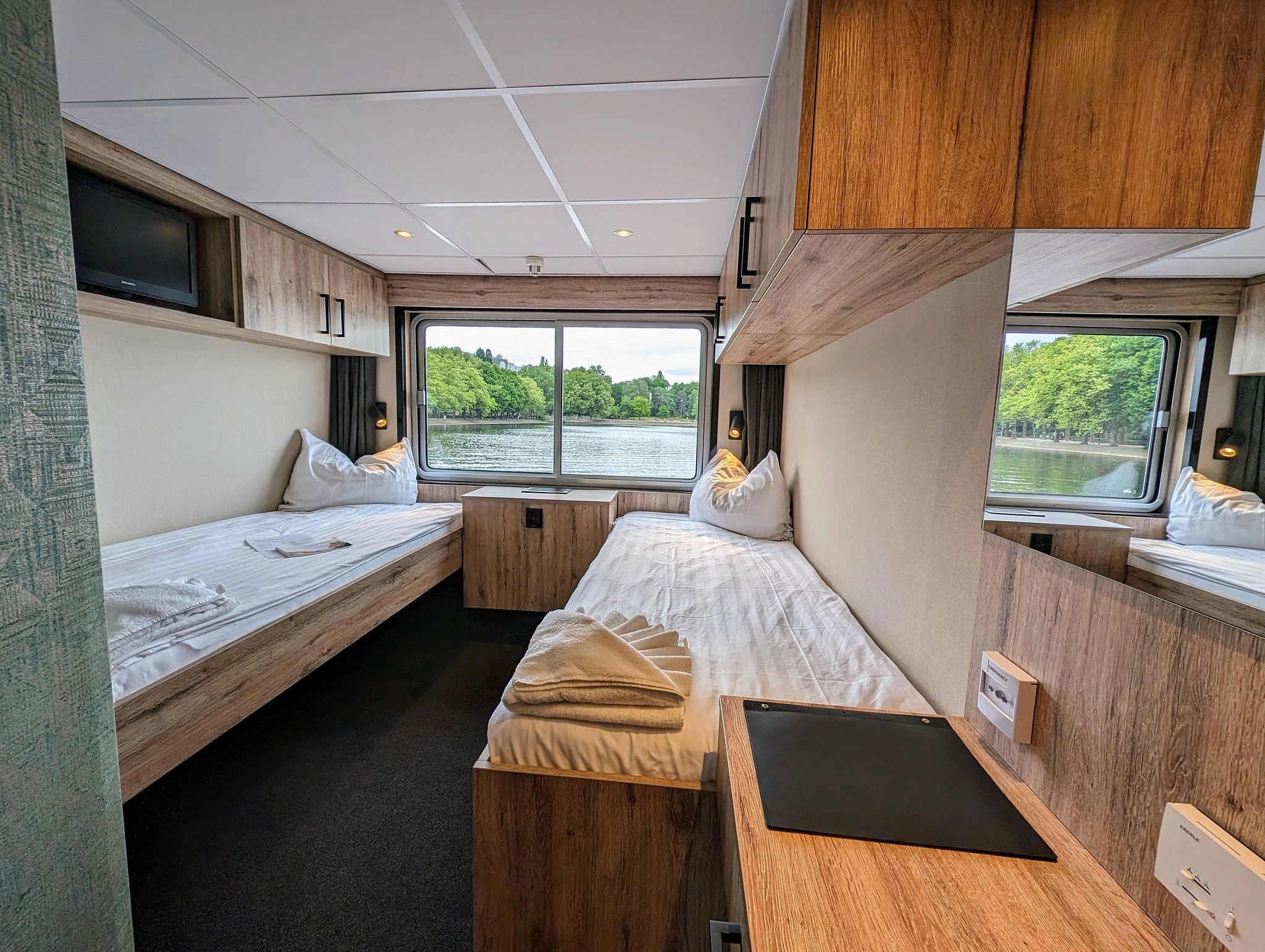 Comfortable upper deck twin cabin on the MS Princess with two separate beds, modern wooden interior, and a large panoramic window overlooking the river.