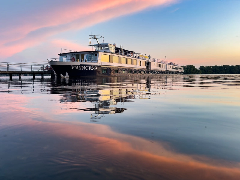 MS Princess sailing on the Oder River at sunset, with reflections in the water.