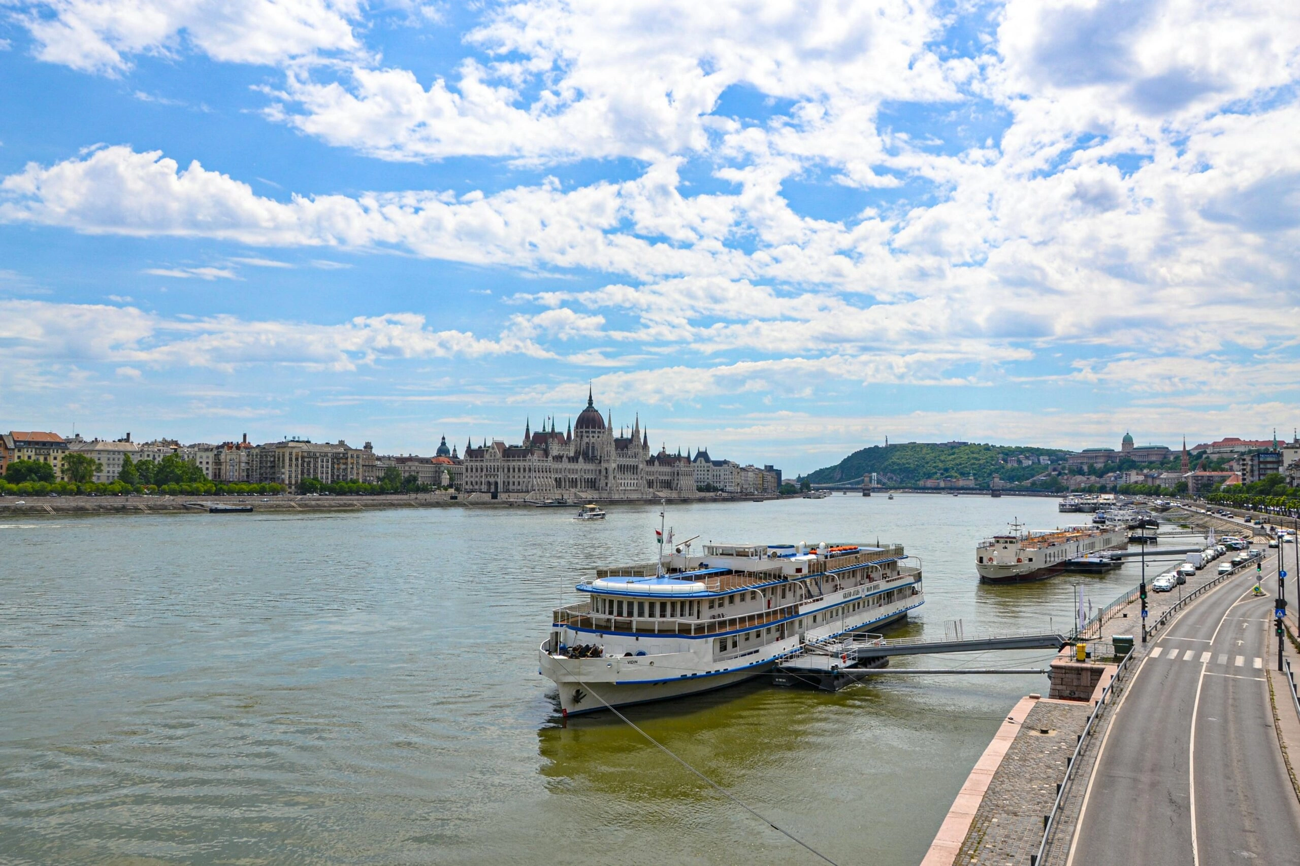 Riviercruises op de Donau met het Hongaarse Parlementsgebouw aan de oever in Boedapest onder een blauwe lucht met wolken.