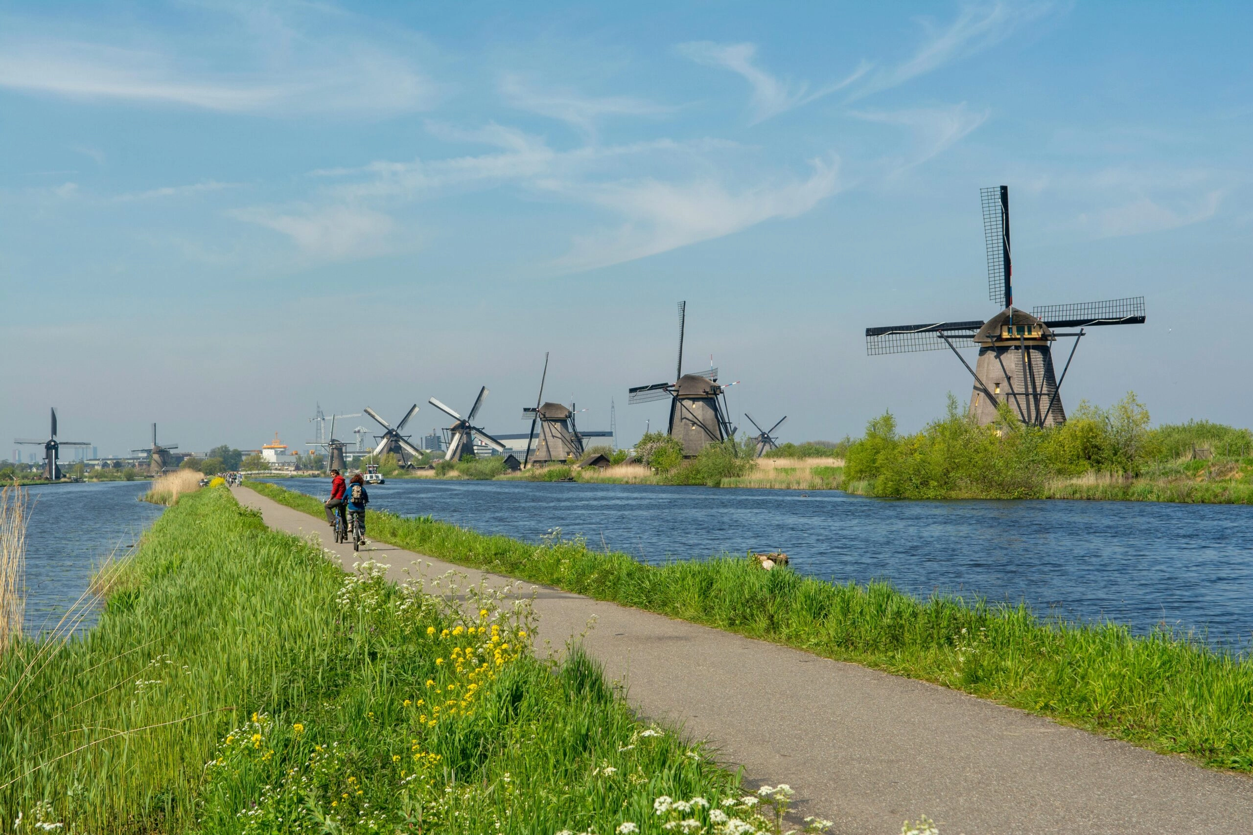 Twee fietsers op een dijkpad langs de molens van Kinderdijk tijdens een fietsvakantie in Nederland
